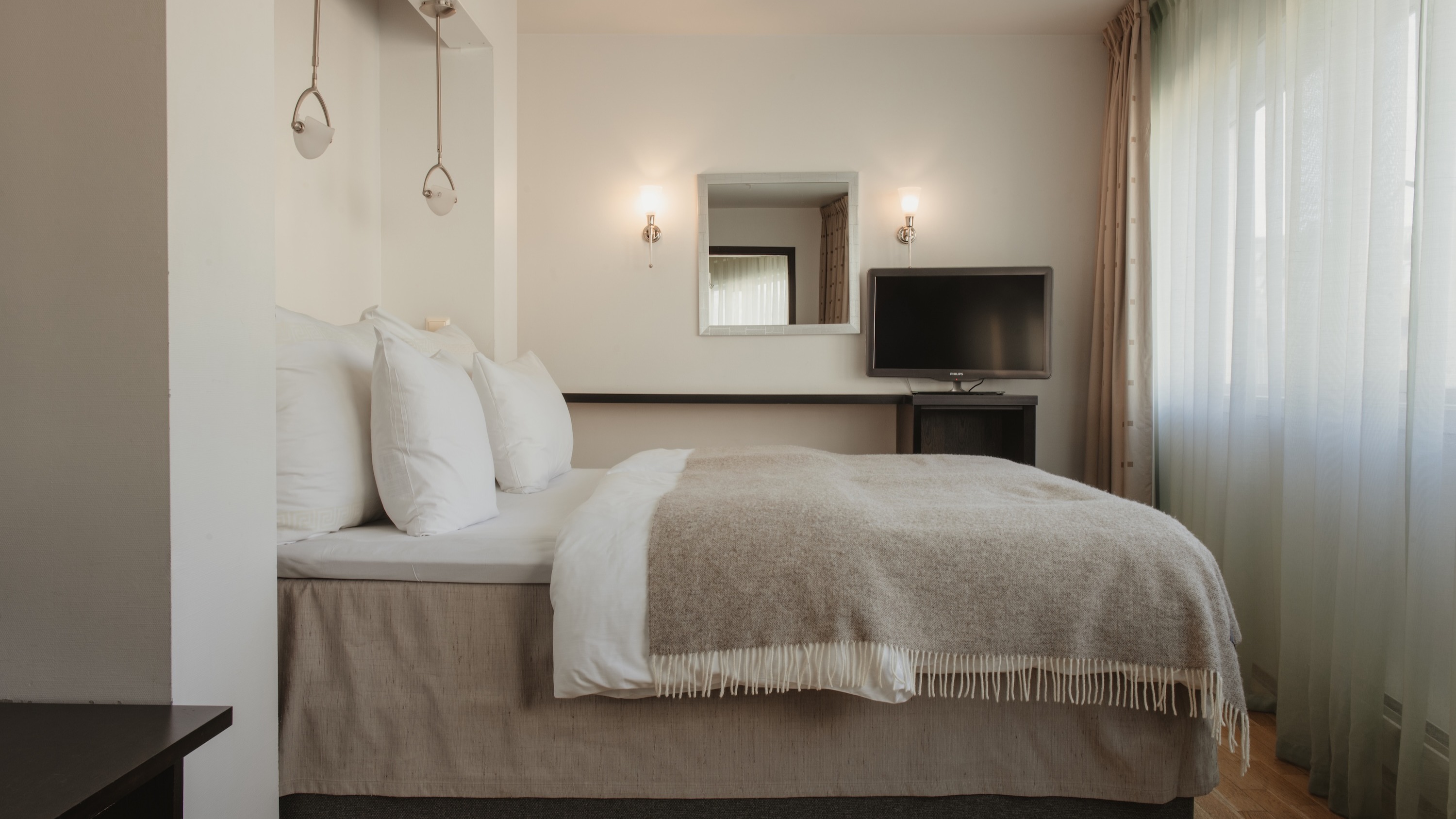 Ett mysigt hotellrum med en säng, en TV och ett fönster med skira gardiner.