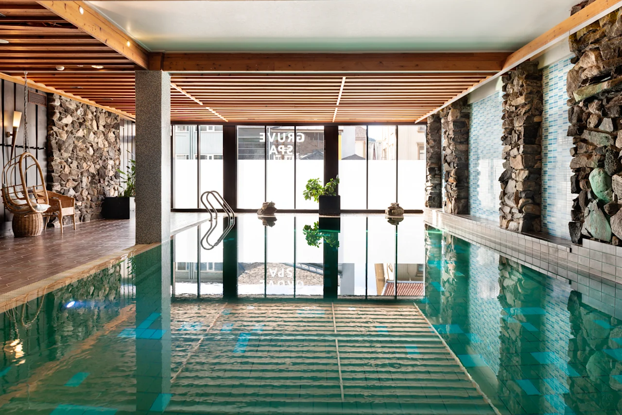 Indbydende indendørs poolområde på Quality Hotel Grand, Kongsberg, med naturligt lys, stenmure, hyggelig siddeplads og Grand Spa-reflektioner.