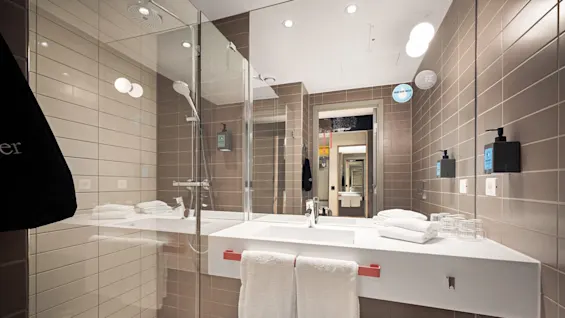 A modern bathroom features a spacious glass shower, double sink with towels and toiletries, and beige tiled walls. Text includes "DRINK TAP WATER" and "GO EASY ON THE PLANET."
