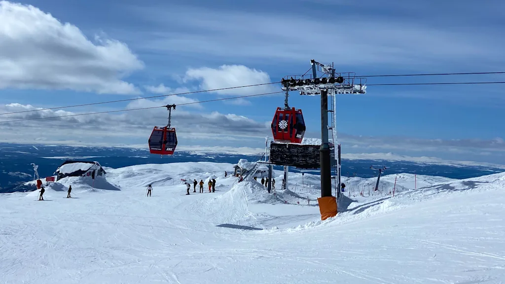 Skiers and snowboarders enjoying a sunny day on a snowy mountain with red gondolas overhead.