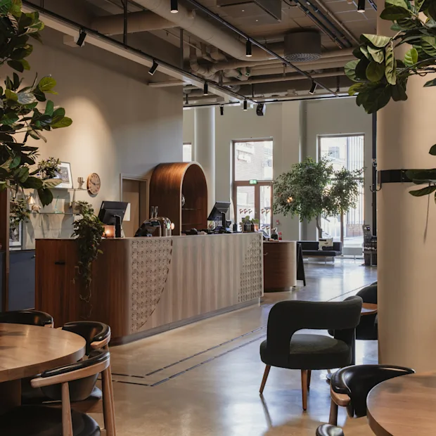 Home Hotel Tapetfabriken: A modern and inviting hotel lobby with a wooden reception desk, comfortable seating, and lush green plants.