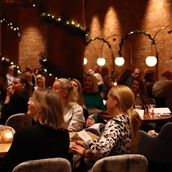 En grupp människor samlade i en varm, inbjudande lokal, som uppmärksamt tittar på ett evenemang eller en presentation.