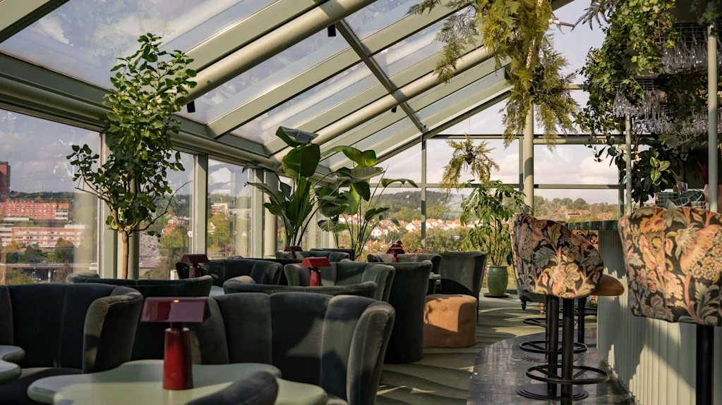 Tyylikäs kattolounge lasikatolla, rehevällä kasvillisuudella ja mukavilla istuimilla, tarjoten panoraamanäkymät kaupunkiin.