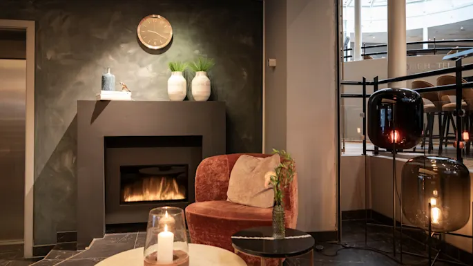 A warm and inviting hotel lounge with a lit fireplace and comfortable seating. Home Hotel Grand Bodø.