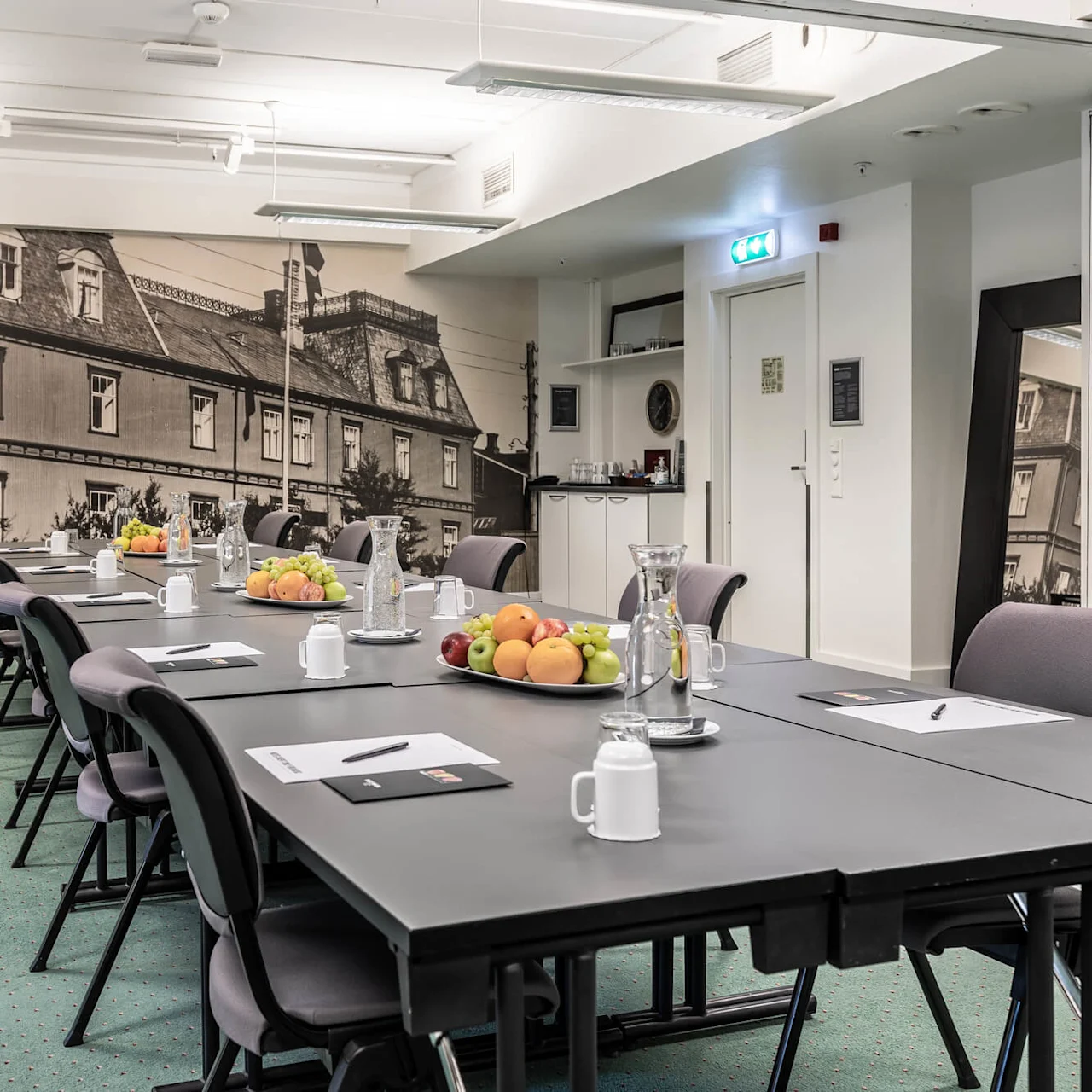 A conference room with a long table set for a meeting, chairs around it, and a large photo of a building on the back wall.