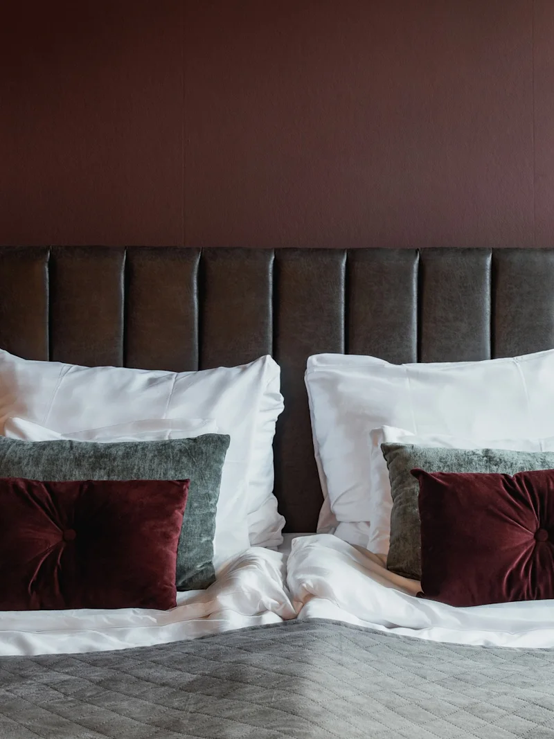 En mysig sovrumsscen med en prydligt bäddad säng med mjuka kuddar och varm belysning, inbjudande till avkoppling.