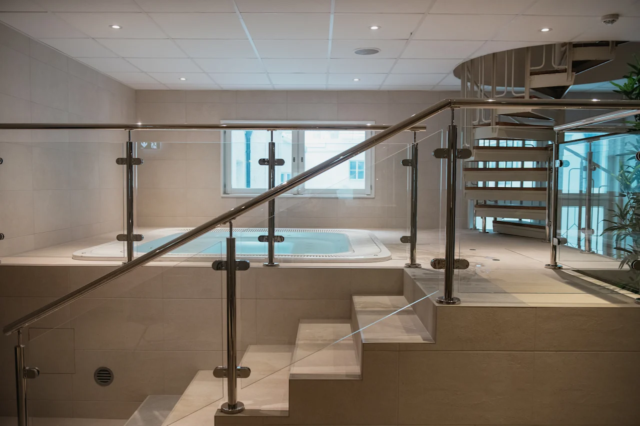 Sisätilojen spa-alue, jossa on poreallas, modernit lasikaiteelliset portaat ja kierreportaat taustalla.