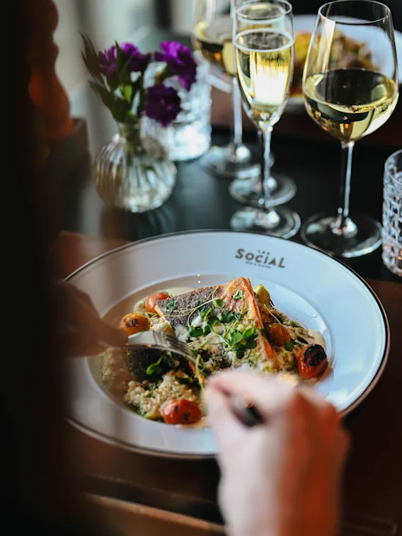 A person enjoying a delicious fish dish with white wine at a restaurant table