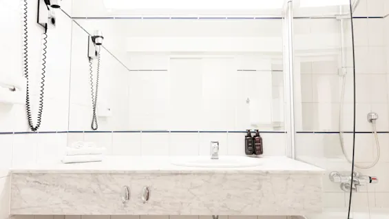 A well-lit bathroom with a white tiled shower and a vanity area, equipped with a hairdryer and toiletries for guests.