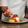 A chef using tweezers to carefully garnish a beautifully plated fish dish.