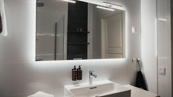 Et moderne badeværelse med et stort, baggrundsbelyst spejl over en slank vask, der tilbyder et lyst og funktionelt rum.