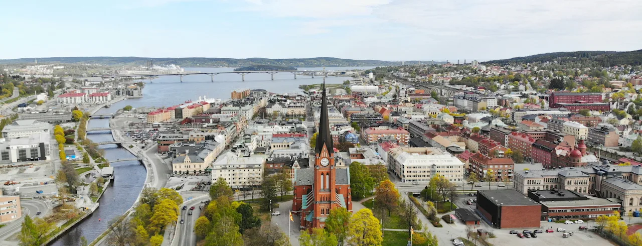 Ilmakuva Sundsvallin kaupungista, jossa on merkittävä kirkko, joki, sillat ja kaupunkimaisema pilvisen taivaan alla.