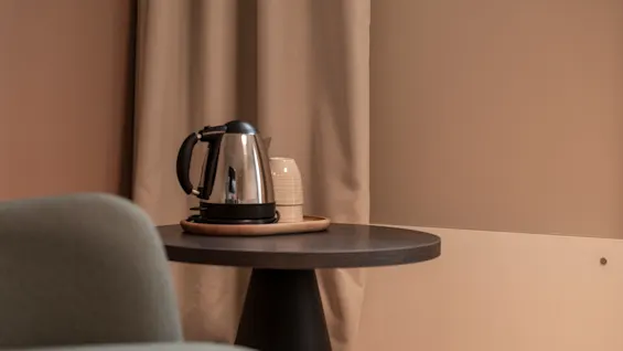 A chrome electric kettle and cups on a tray on a round table, ready for a warm drink in a cozy room.