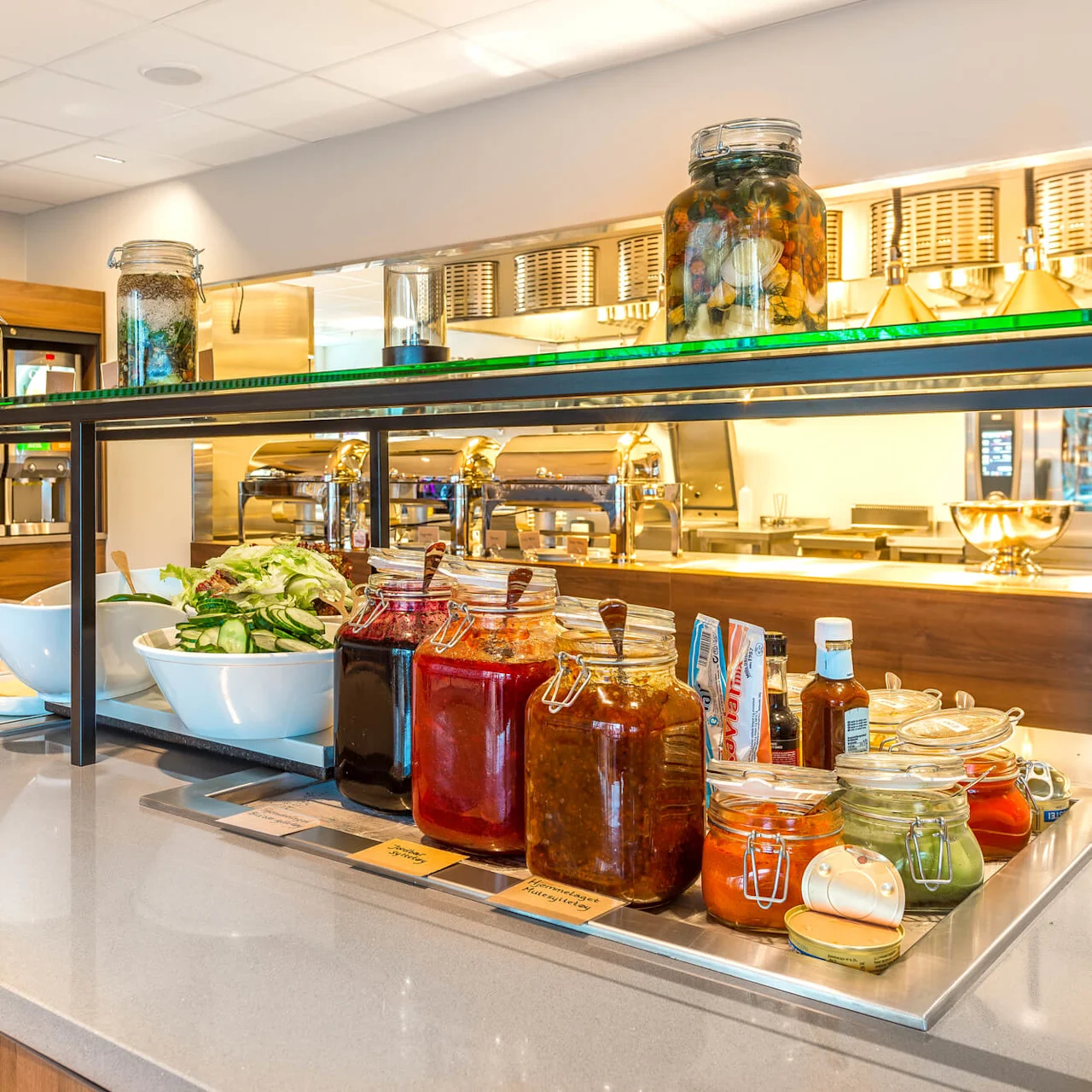 Itsepalvelubuffet erilaisilla ruoilla ja lisukkeilla, valoisassa kafeteriassa.