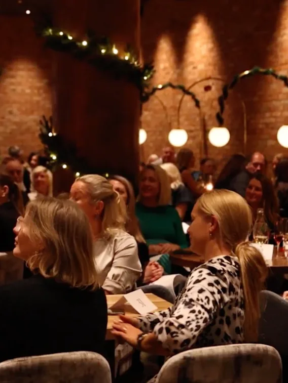 En grupp människor samlade i en varm, inbjudande lokal, som uppmärksamt tittar på ett evenemang eller en presentation.