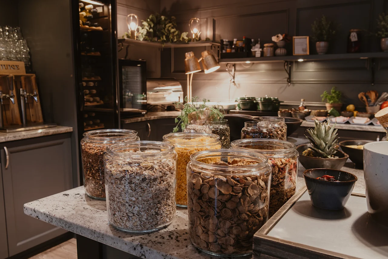 A breakfast buffet at Home Hotel Kung Oscar with various cereals and nuts in glass jars, and a juice dispenser labeled JUICE.