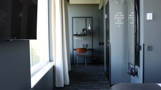 A modern hotel room with a desk, a window, and a wall message that reads: IF YOU CANT FIND THE BUTLER DO IT YOURSELF.