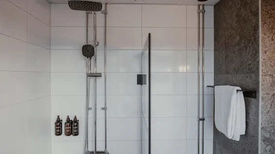 Puhdas ja kutsuva suihkutila, jossa on valkoiset laatat, sadesuihku ja hygieniatuotteet, valmiina virkistävään pesuun.