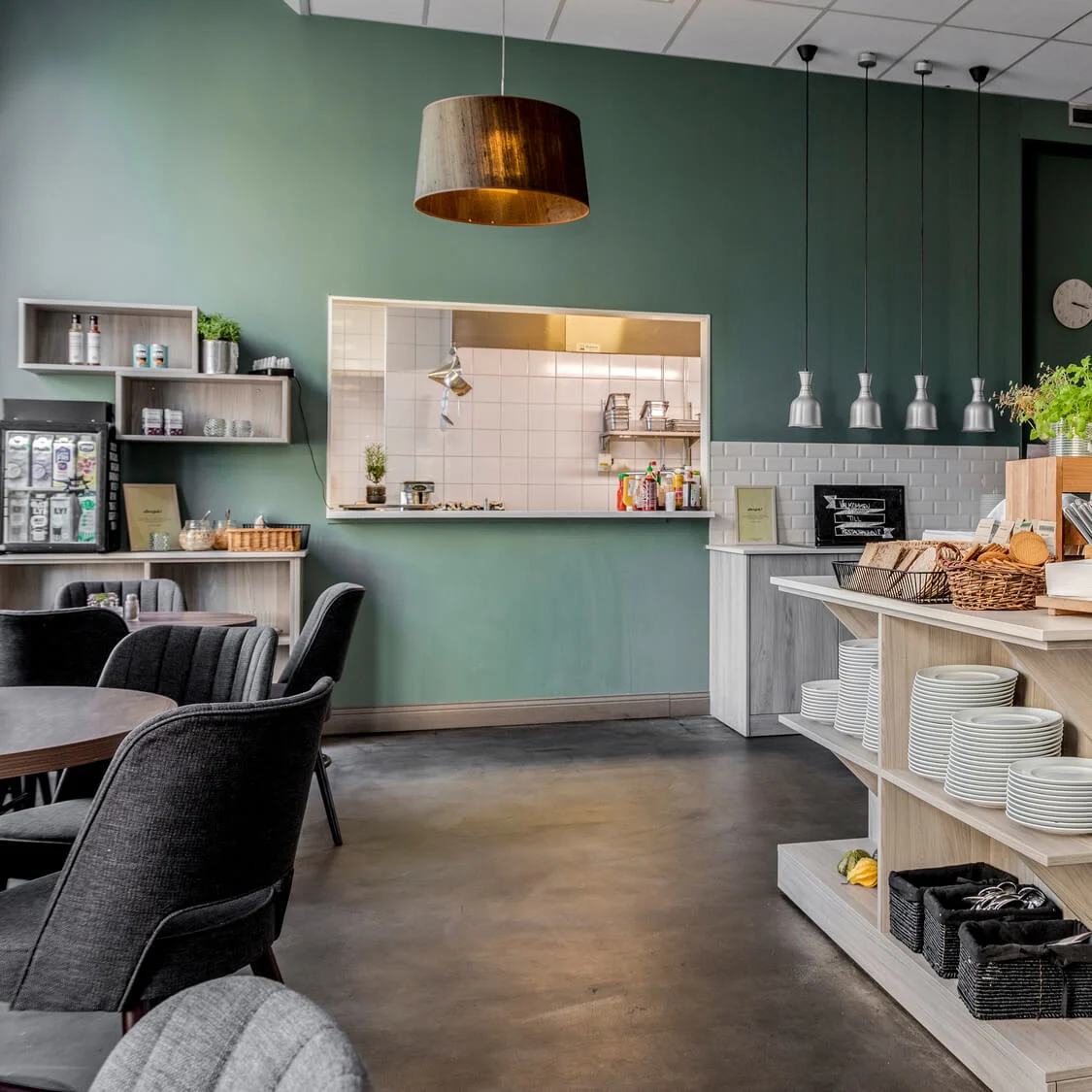 Modern café interior with a serving counter, shelving with crockery and plants, in a cozy atmosphere.