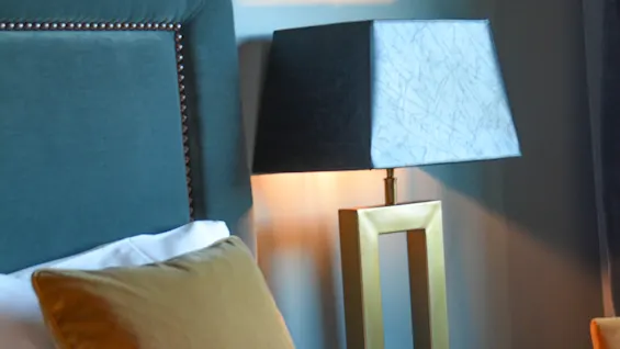 Seng med en blød pude, ved siden af en moderne lampe, der gløder blødt, placeret i et hyggeligt soveværelse med mørk sengegavl og dæmpede farver.