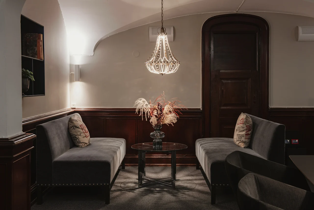 En inbjudande lounge med plyschsoffor, ett soffbord prytt med blommor och en gnistrande ljuskrona. Home Hotel Grand, Helsingborg.