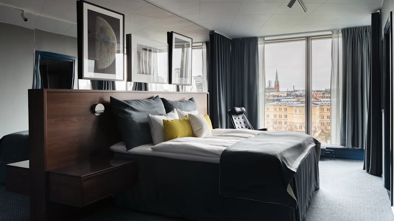 Moderni hotellihuone mukavalla sängyllä ja kaupunkinäkymällä. Stratum Suite by Bernadotte ja Kylberg Clarion Hotel Signissä.