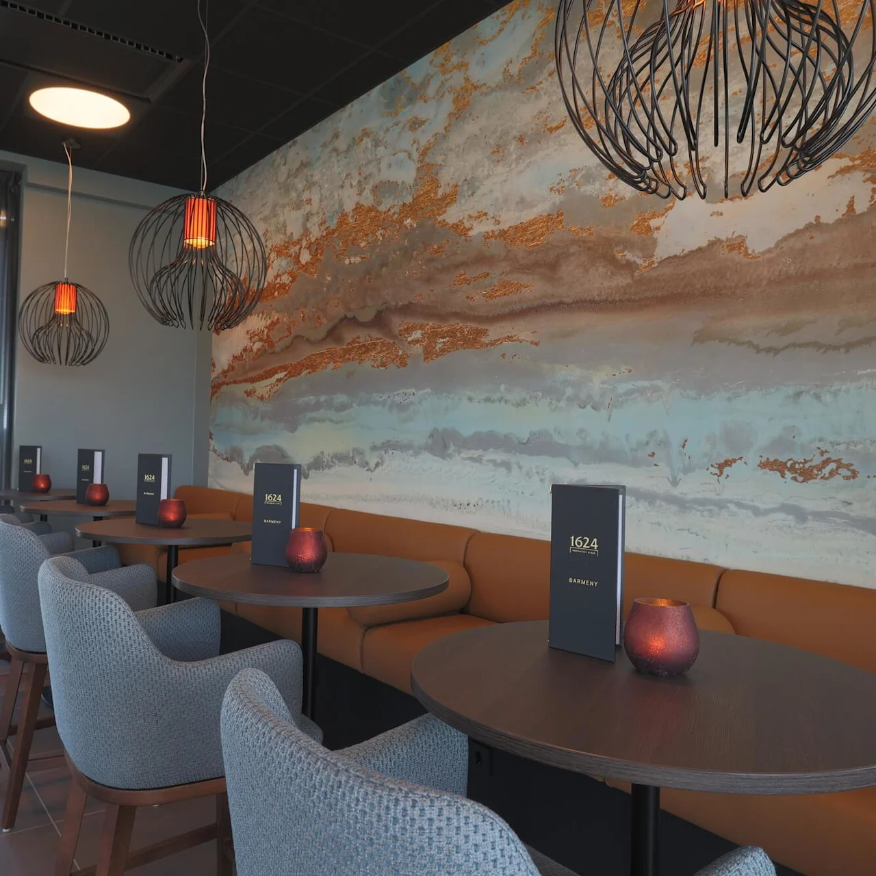 Round dining tables surrounded by upholstered chairs, large abstract wall art, modern light fixtures; tranquil, stylish restaurant setting.
