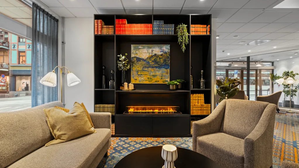 En mysig hotellounge med en bekväm sittgrupp, ett soffbord och en stilren bokhylla med en varm öppen spis.
