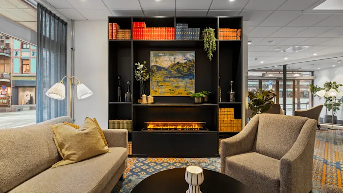 En koselig hotellounge med et komfortabelt sitteområde, et salongbord og en stilig bokhylle med en varm peis.