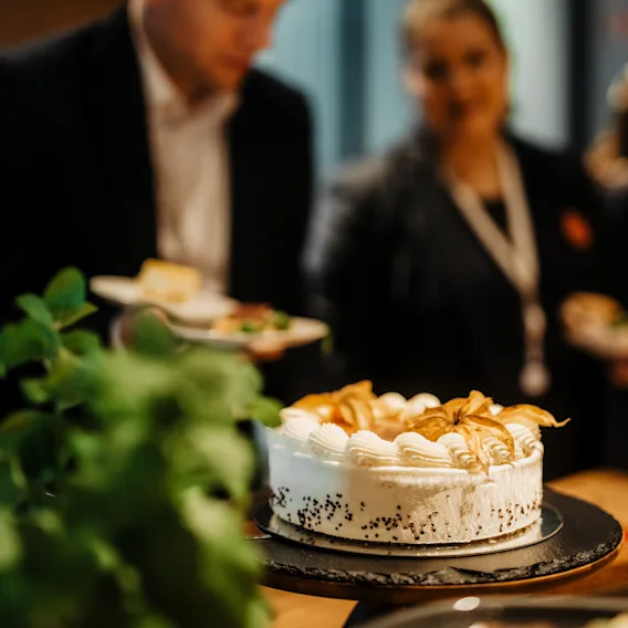 Osallistujat nauttivat virvokkeista, kauniisti koristeltu kakku etualalla, konferenssissa Clarion Hotel Helsinki Airportissa.