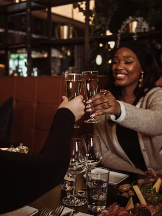 Two people toasting with champagne glasses in a cozy restaurant setting, enjoying a meal together.