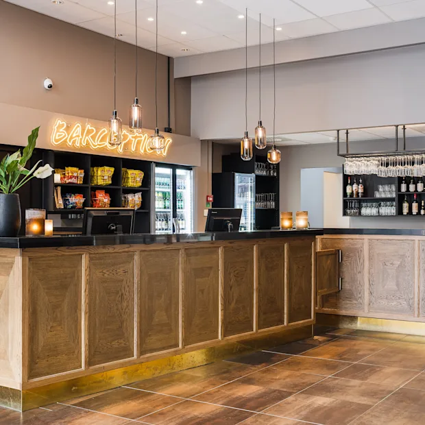 Modern hotel reception and bar in light wood with a glowing Barception sign on the wall.