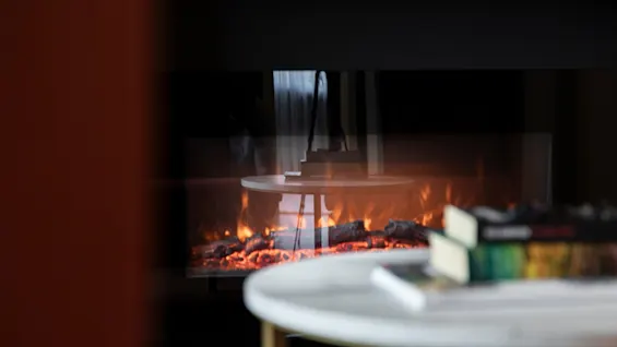 A cozy fireplace scene at Home Hotel Grand Bodø, with a table and books in the foreground, creating a warm ambiance.