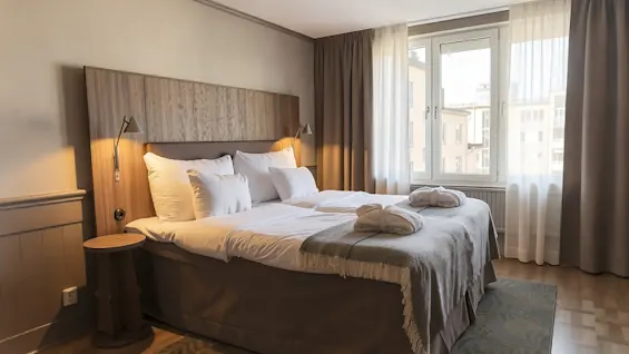 Ett mysigt hotellrum på Home Hotel Tapto med en stor säng, vita sängkläder, badrockar och ett fönster med utsikt över stadens byggnader.