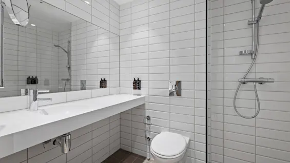 Ett ljust och modernt badrum med vita kakelplattor, en elegant kommod med handfat, en toalett och en duschkabin.