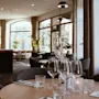 Elegant dining table set with wine glasses and napkins in a modern restaurant; soft lighting creates a warm ambiance. "SICH" text visible on napkin. Large windows reveal trees outside.  