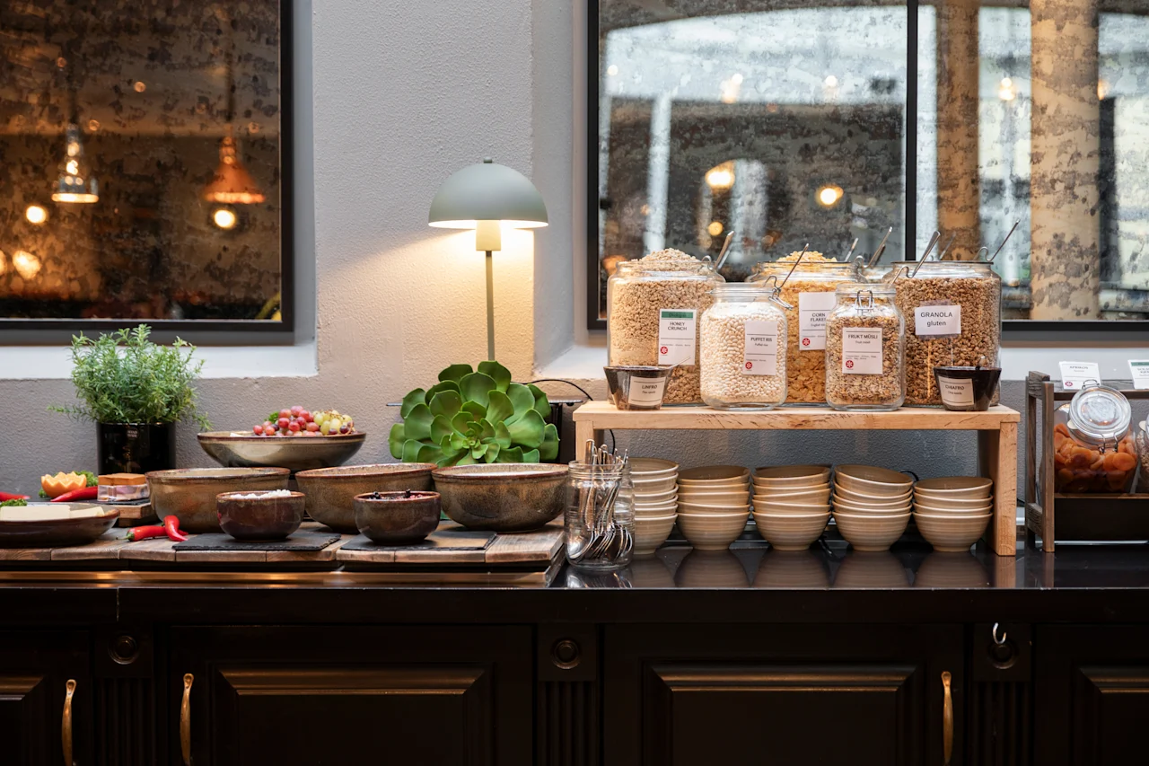 Home Hotel Grand Bodø breakfast buffet with cereals like GRANOLA gluten, FRUIT MUESLI, POPPED RICE, HONEY CRUNCH, and fresh fruit.