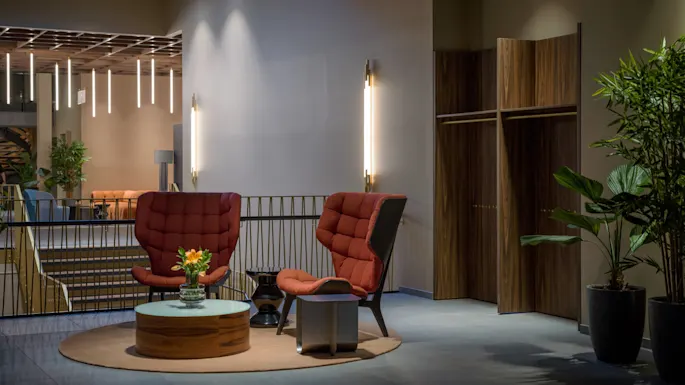 Kaksi verhoiltua tuolia on vastakkain pyöreän pöydän kanssa, johon on asetettu kukkia. Ne ovat modernissa oleskelutilassa kasveilla ja valaisimilla.