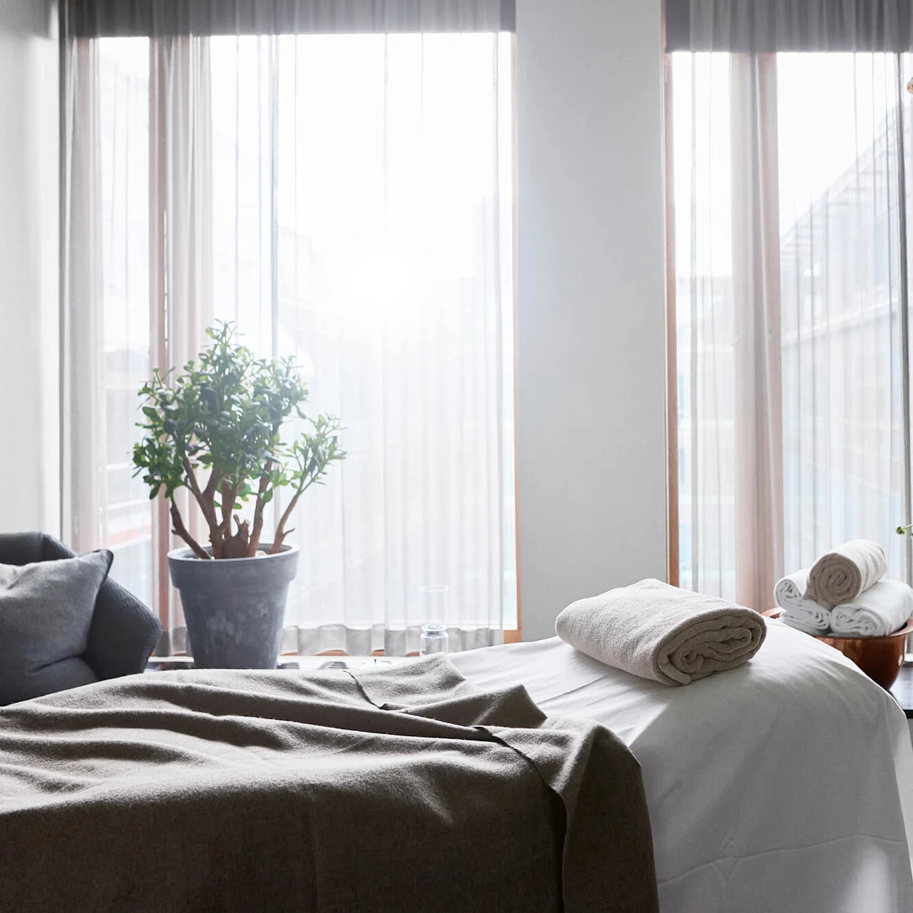 A neatly made bed with towels, next to a window letting in daylight, in a tidy room.