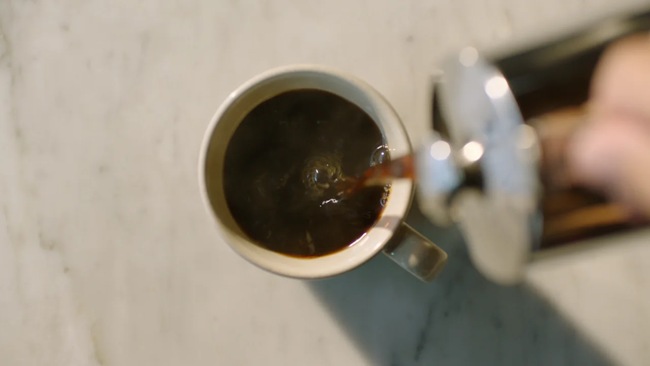 Coffee being poured from a French press into a mug, seen from a top-down view.