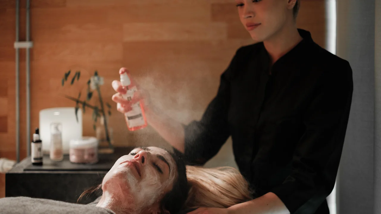 En person som får en ansiktsbehandling, med en spa-professionell som försiktigt sprejar deras ansikte.