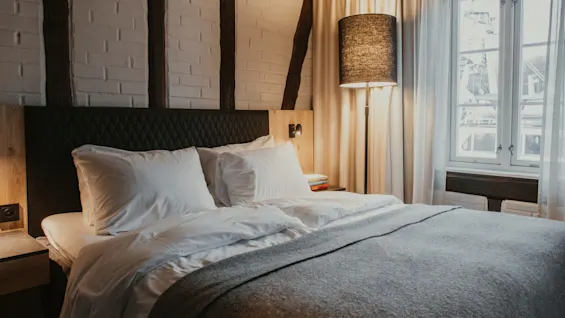 Et komfortabelt og indbydende hotelværelse, klar til afslapning, med en blød seng, varm belysning og udsigt til ydersiden.