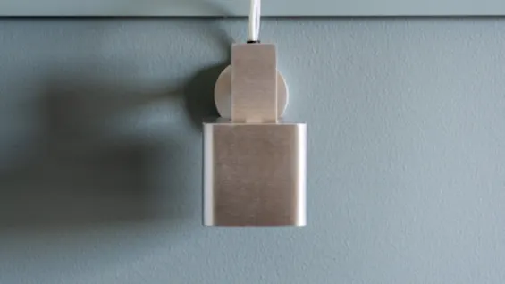 Et børstet metallobjekt med en hvit kabel plugget inn i en tofarget vegg, lyseblå-grå nederst og off-white øverst.
