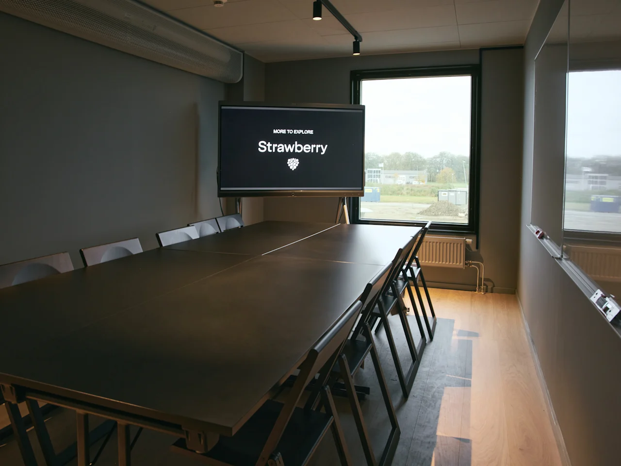 Et moderne konferanserom på Stopover Hotel Falkenberg med en stor skjerm som viser "MORE TO EXPLORE" og et langt bord med stoler.