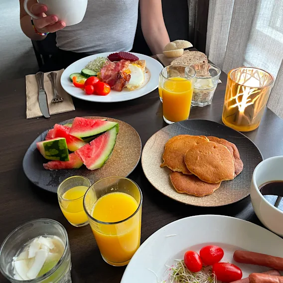 Frokostbord fylt med pannekaker, vannmelon, appelsinjuice, kaffe, bacon og egg.