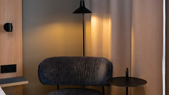 A cozy hotel room corner with a comfortable chair, warm lamp light, and a small table, perfect for relaxation.