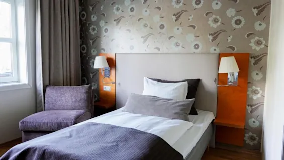 Et koselig hotellrom på Clarion Hotel Oslo Airport med en komfortabel seng, en lilla stol og blomstret tapet.