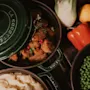 A delicious meal being served at Home Hotel Kung Oscar, featuring a pot of meat with LA COCOTTE, mashed potatoes, and peas. Fresh vegetables are on the side.