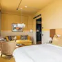 Et levende hotelværelse på Hernö Gin Hotel med en hyggelig seng, en komfortabel gul sofa og moderne indretning.