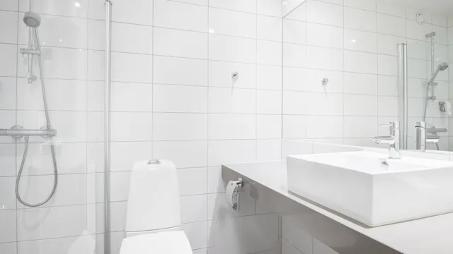 Toalett och handfat står i ett rent, modernt badrum med vita kakelväggar och ett duschområde, vilket skapar en minimalistisk och funktionell yta.